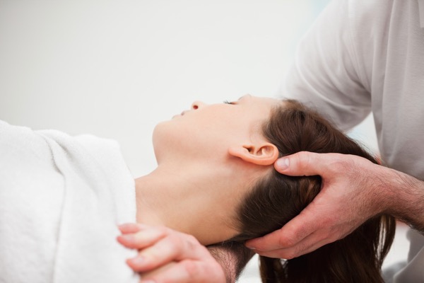 Osteopath stretching neck of patient with headache, neck and shoulder pain